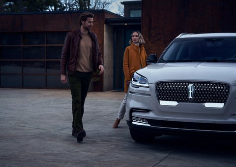 A man and a woman approaching a 2024 Lincoln Aviator® SUV, which illuminates certain lights when they are close | Griffin Lincoln in Tifton GA